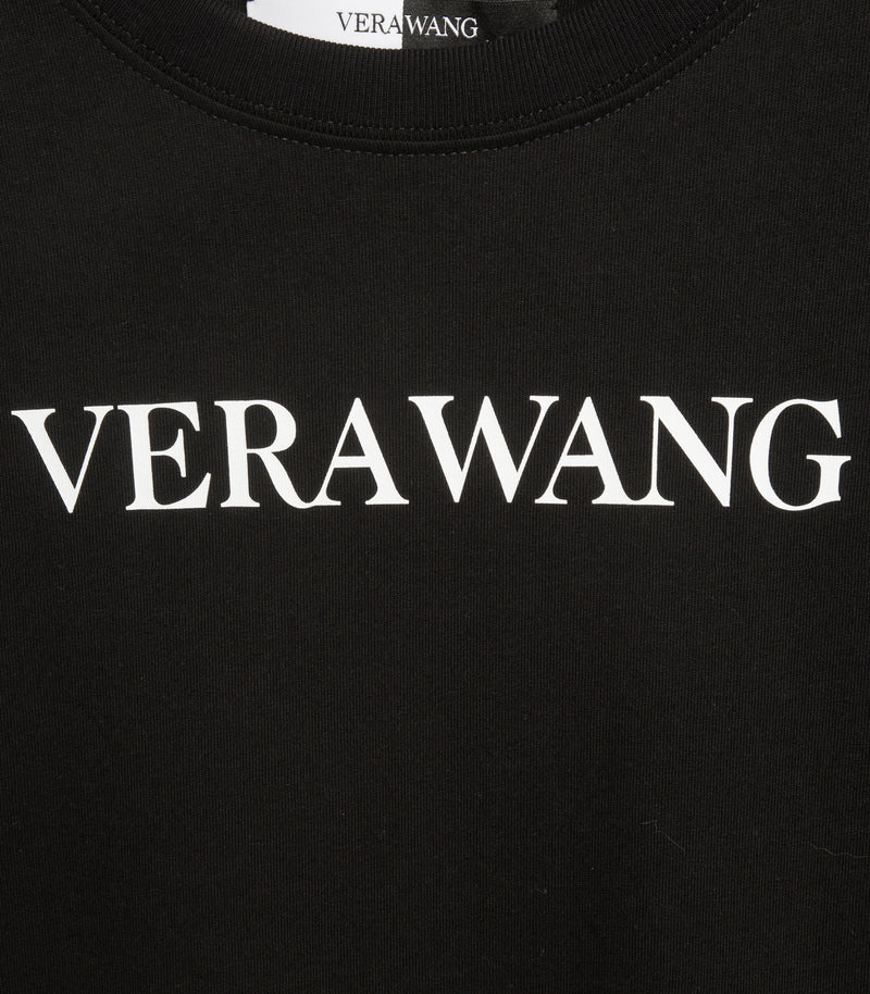 Close-up detail of a black crewneck t-shirt showcasing the 'VERA WANG' brand logo printed in white across the chest, with a glimpse of the ribbed neckline and inner woven brand label.