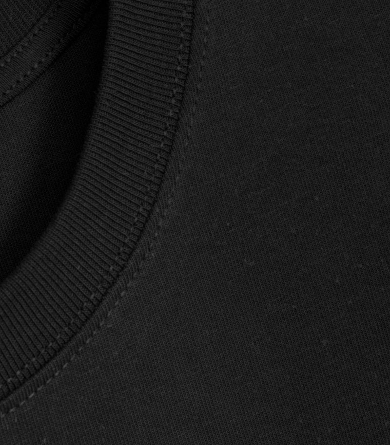 Close-up product view of a black crewneck t-shirt, highlighting the fine texture of the premium cotton jersey fabric, the tight ribbing on the collar, and the clean tonal topstitching along the neckline seam.