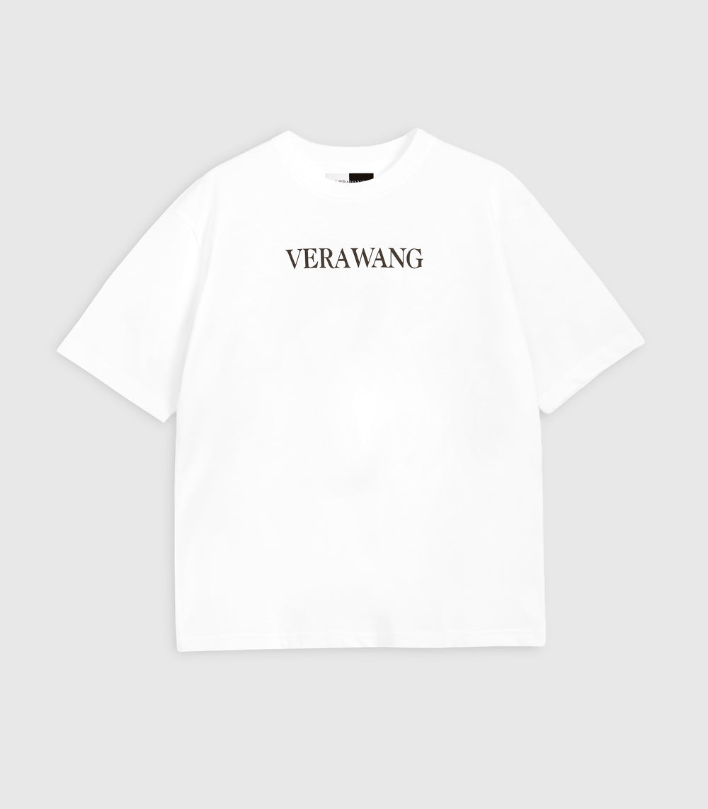 Flat lay product view of a relaxed, loose-fit white cotton t-shirt featuring the minimal 'VERA WANG' logo printed in black across the upper chest, complete with wide short sleeves, a classic crew neckline, and a visible split black-and-white inner neck label against a light grey background.
