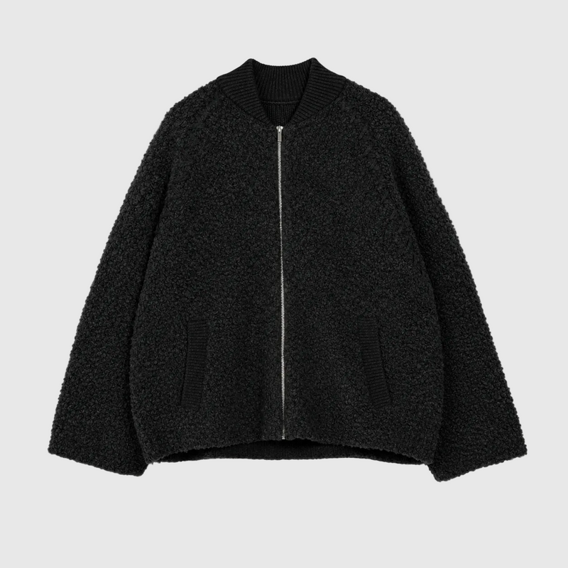 A black textured bouclé zip-up jacket with a ribbed knit collar, laid flat against a light gray background.
