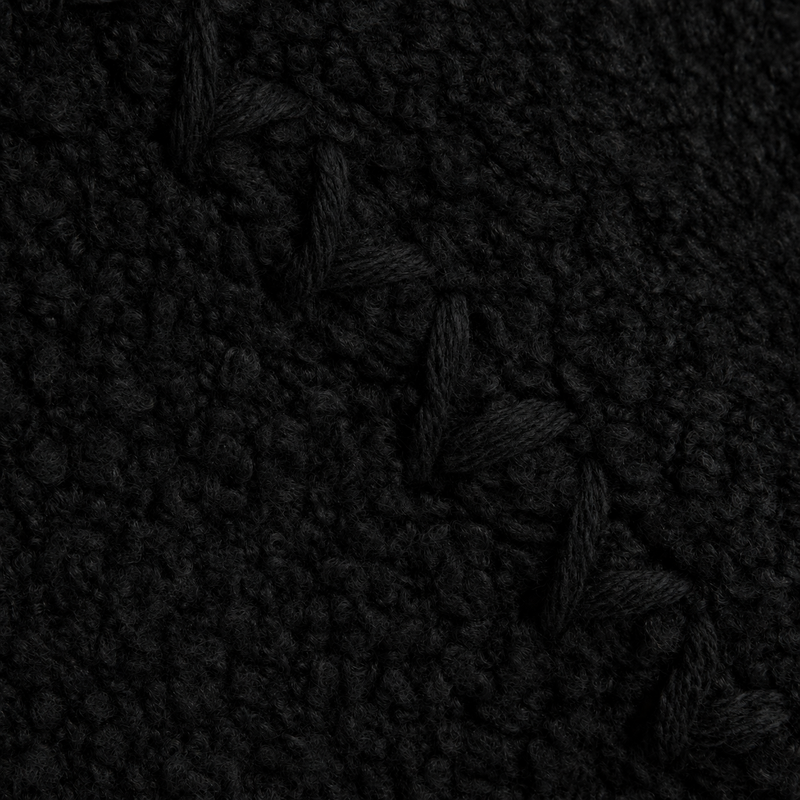 A close-up of a black textured knit fabric with a braided cable pattern.