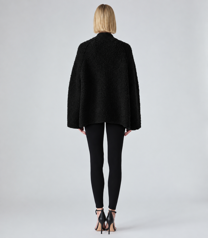 A model shown from the back wearing a black textured boucle jacket, black leggings, and black high-heeled sandals against a light gray studio background.
