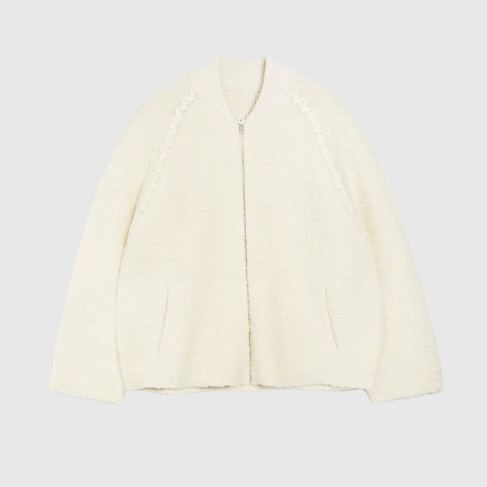 An off-white textured zip-up cardigan with decorative zig-zag knit patterns on the chest and two front pockets, shown on a plain white background.