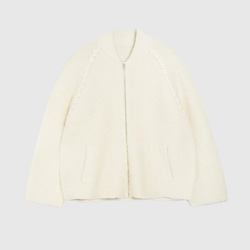 An off-white textured zip-up cardigan with decorative zig-zag knit patterns on the chest and two front pockets, shown on a plain white background.