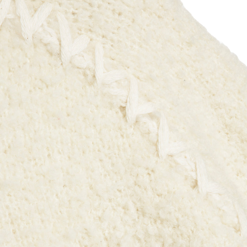 Close-up of a cream-colored knit fabric with a braided or knotted trim detail running diagonally across the surface.