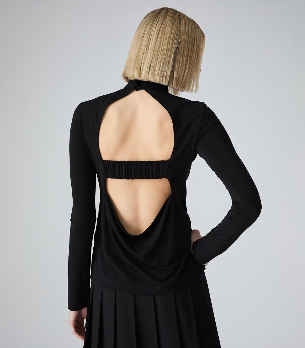 A woman shown from the back wearing a black long-sleeve dress with a large open back and a gathered elastic band across the upper back, against a light gray studio background.