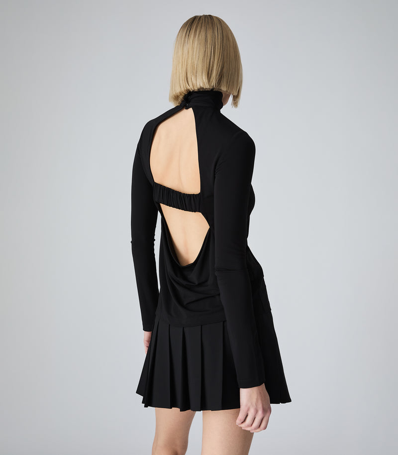 A model from the back wearing a black long-sleeve mini dress with a high neck and a large open back design, set against a plain light gray studio background.