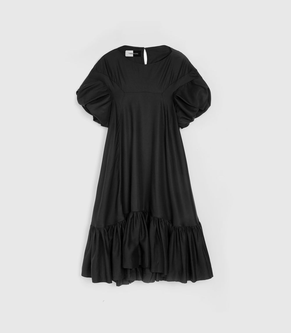 Flat-lay view of a knee-length black smock dress featuring a relaxed, voluminous silhouette, a high boat neckline, and dramatic gathered ruffle short sleeves. The dress is constructed with a distinctive square chest yoke panel and a heavily gathered tiered ruffle hemline, presented flat against a light grey background.