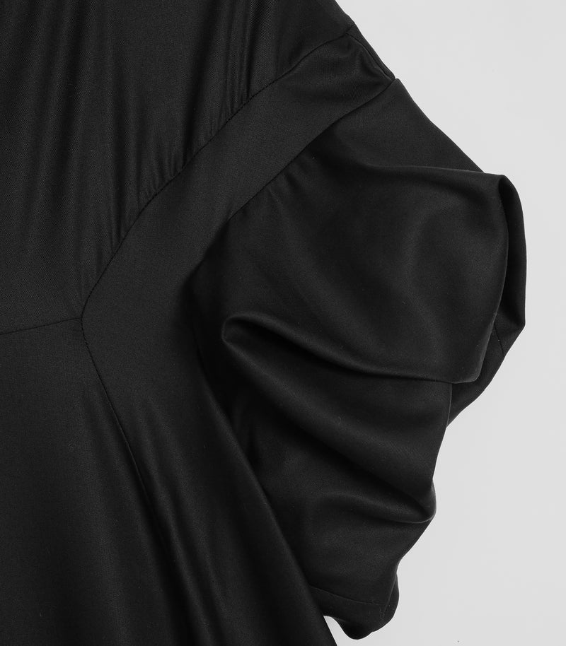 Macro close-up view of the sleeve construction on a black smock dress, highlighting the fine woven fabric texture. The shot focuses on the dramatic, architectural volume of a gathered puffed short sleeve seamlessly integrated into a curved, angled bodice yoke seam.