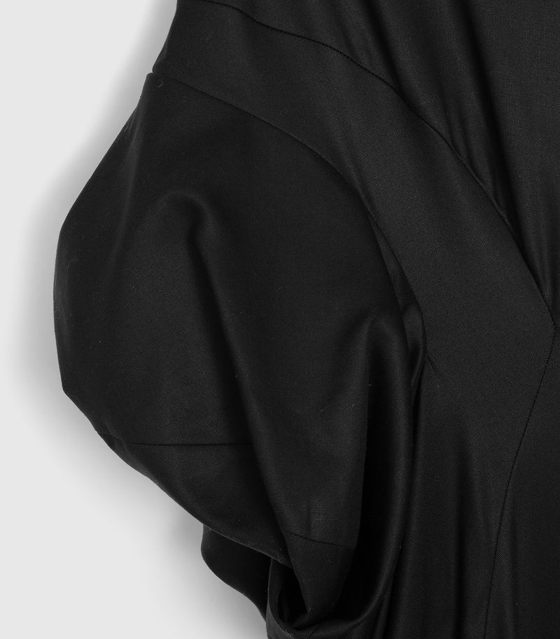 Macro close-up view of the sleeve construction on a black smock dress, highlighting the fine woven fabric texture and subtle diagonal weave. The shot focuses on the architectural, rounded volume of a gathered puffed short sleeve joined to a contoured bodice yoke panel.