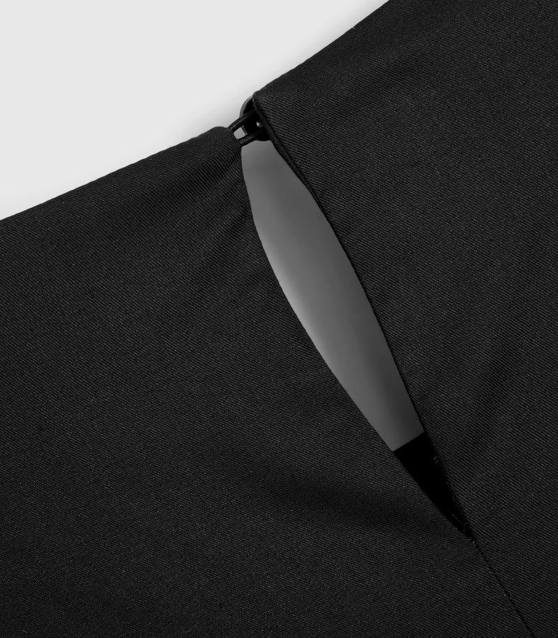 Macro close-up view of the rear neckline on a black smock dress, highlighting the fine woven fabric texture. The shot focuses on a delicate keyhole cutout closure fastened at the top with a small black elastic loop and a subtle hook-and-eye fastening.