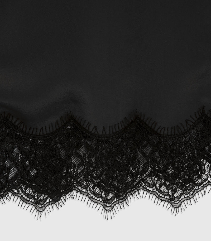 Black lace trim with a scalloped edge and tassel-like fringe, shown against a dark fabric background and a light gray surface below.