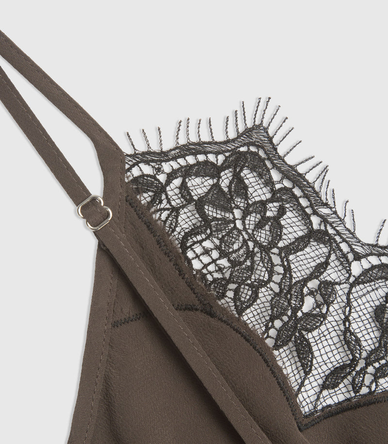 Close-up of a dark brown dress showing the thin shoulder straps, a silver metal adjuster, and a black floral lace underband with fringed edges against a light gray background.