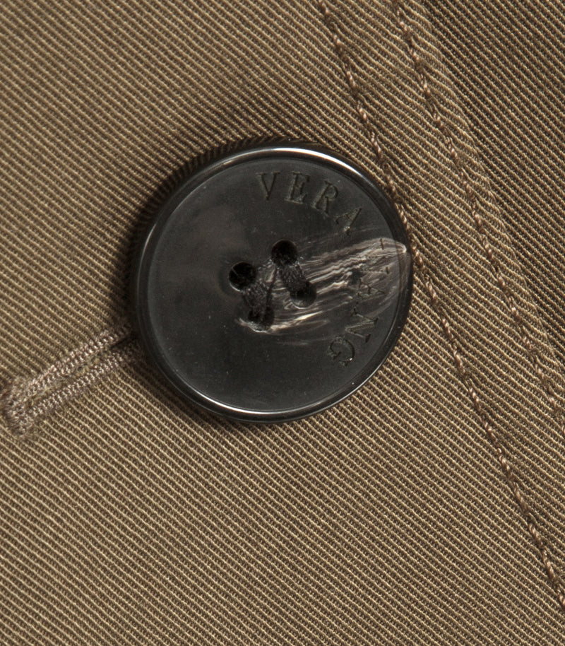 Close-up of a dark brown textured button with two holes on a brown tweed fabric garment, featuring the debossed brand name 'VERA WANG'.
