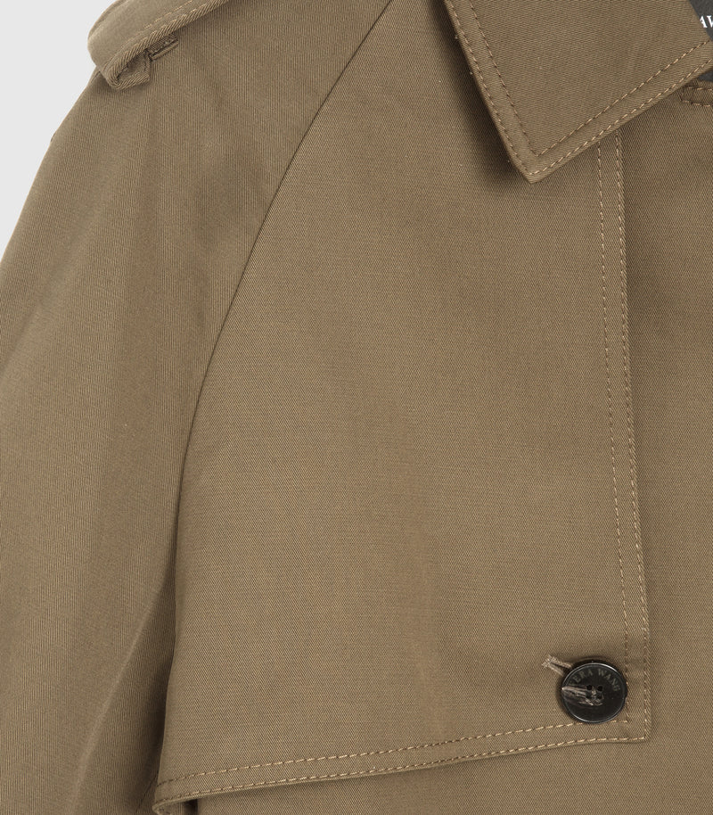 Close-up of a brownish-tan jacket fabric with a collar, buttoned flap pocket, and a dark button on a light gray background.
