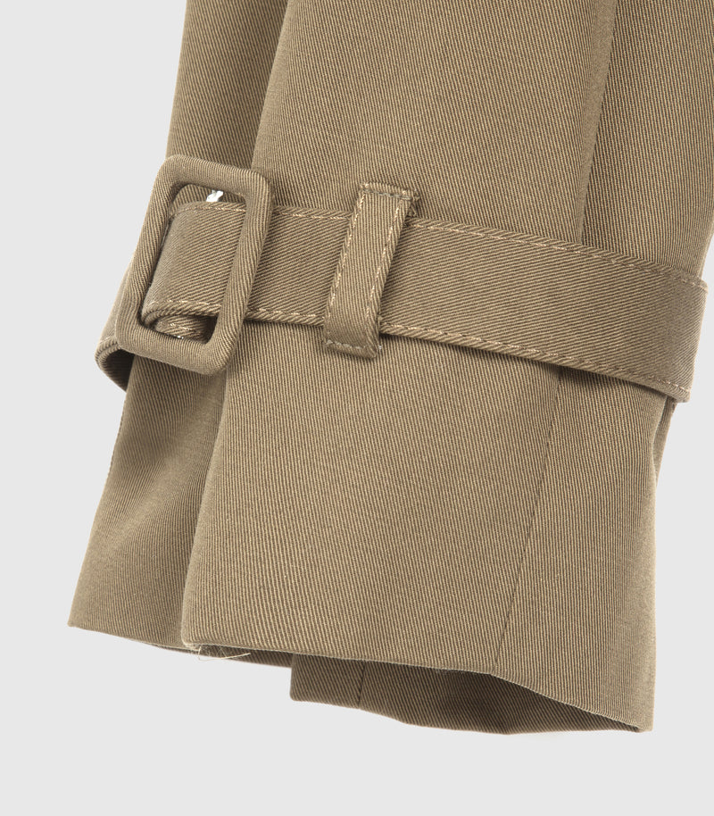Close-up of a beige trench coat sleeve with a matching belt and rectangular buckle, shown against a light gray background.