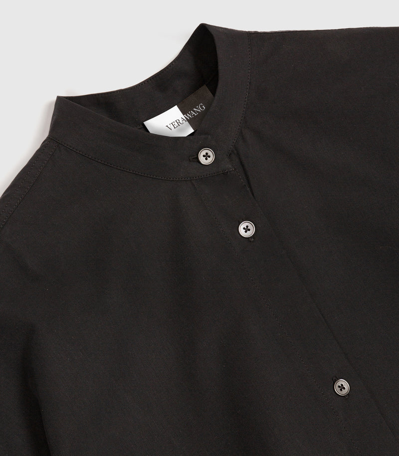 Close-up of a black button-front shirt with a stand collar and visible Black buttons, photographed on a light gray background. A neck label reads VERA WANG.