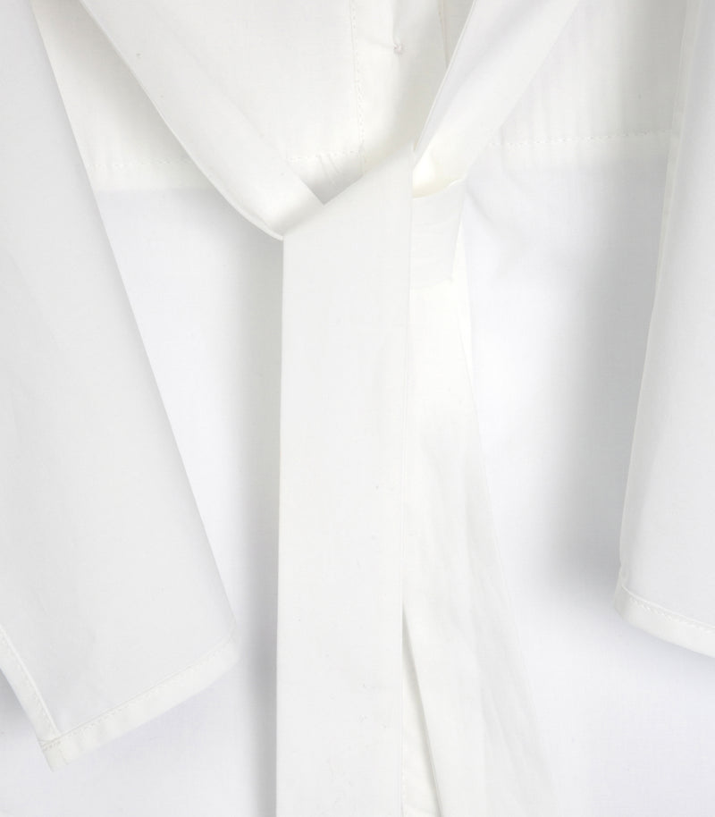 Close-up of a white long-sleeve shirt or robe with a tie-neck detail, showing the fabric texture and folds.