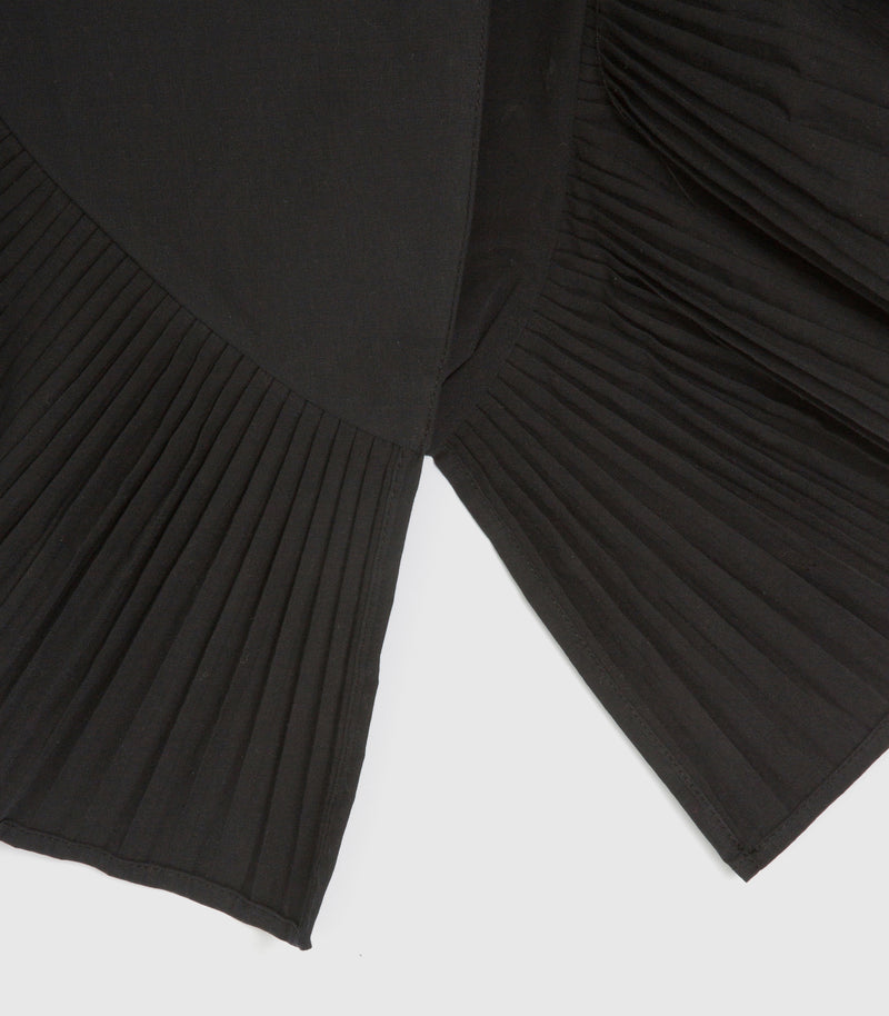 Close-up of a black pleated garment, showing the texture and layered design of the fabric against a light gray background.