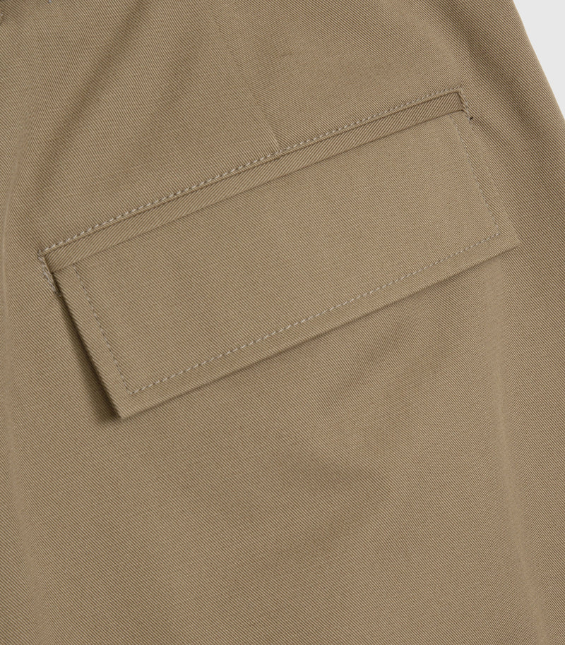 Close-up of a khaki fabric garment showing a rectangular patch pocket with neat contrast stitching.