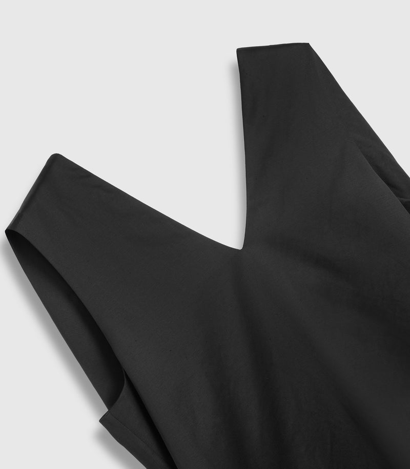 Close-up of a black sleeveless dress with a wide, draped shoulder design and a V-shaped rear neckline, shown on a light gray background.