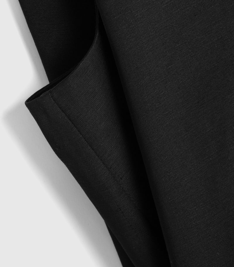 A close-up of a black textured fabric, likely a knit sweater or sweater vest, folded to show its soft texture and drape against a light gray background.